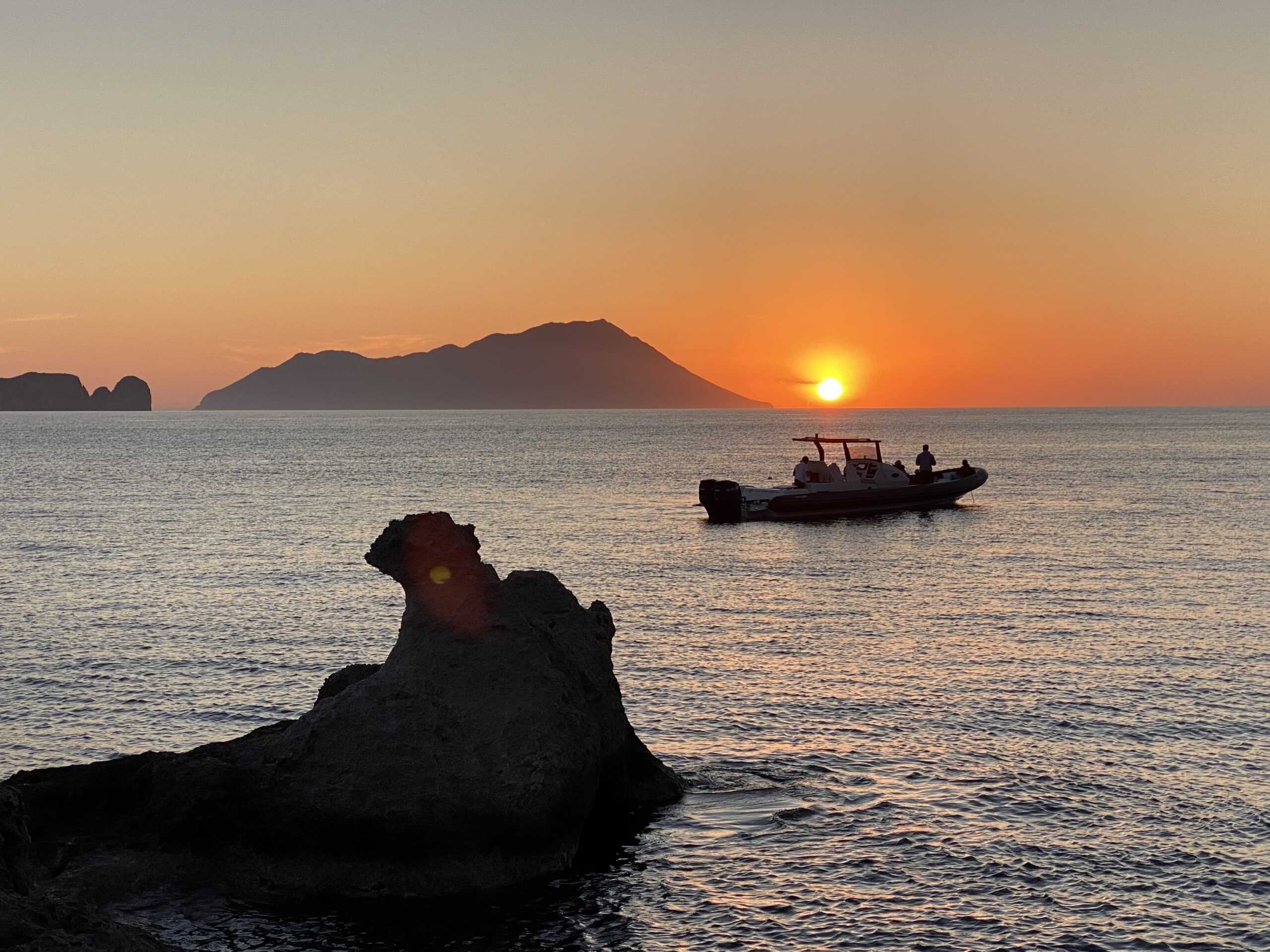 Scenic sunset over calm waters with a boat and silhouette island in the horizon